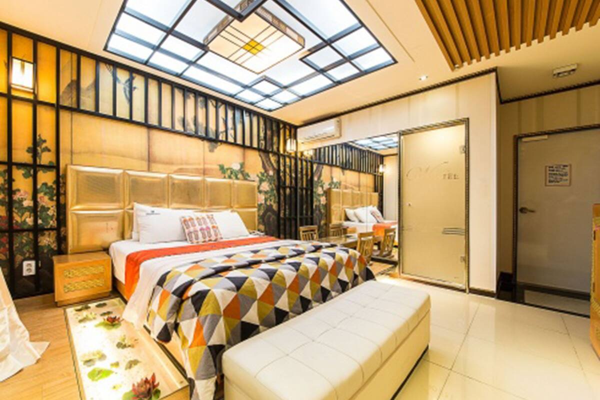 Une chambre moderne avec une lucarne, un grand lit recouvert d’une couette à motifs géométriques, un banc et une petite table agrémentée d’une plante.