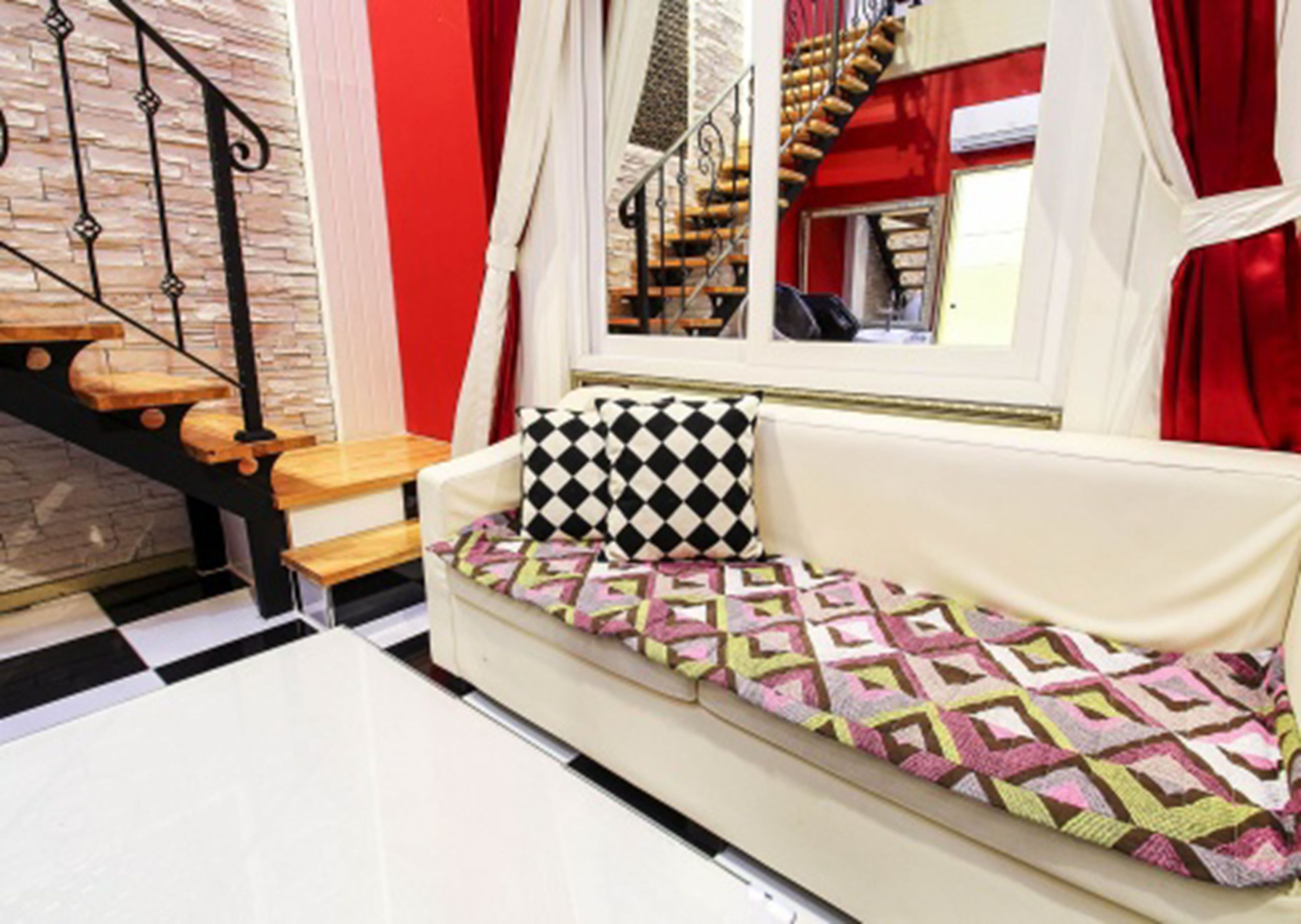 A white sofa with a patterned cushion, a wooden bench, and a staircase with red accents.