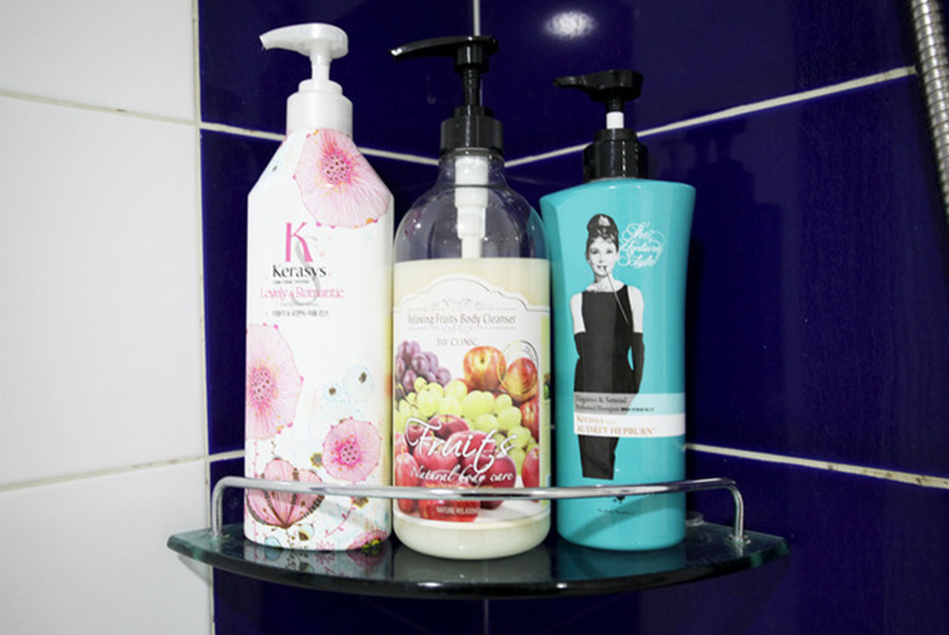 Three bottles of personal care products on a glass shelf against a tiled wall.