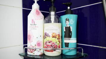 Three bottles of personal care products on a glass shelf against a tiled wall.