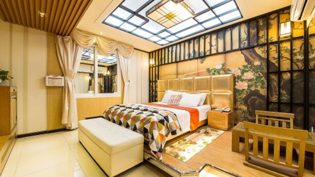 A bedroom with a skylight, a bed with a patterned bedspread, a wooden bench, and a traditional-style wall with artwork. - Belita N Goodtime Drive-in Motel (Paju)