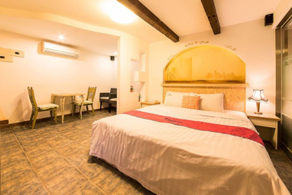 Une chambre d’hôtel avec un grand lit, un bureau, deux chaises, un miroir et un climatiseur fixé au mur.