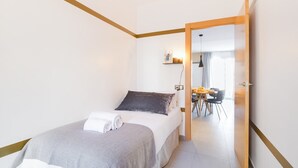A bedroom with a bed, a bedside table, a nightstand, and a door leading to a dining area. - Sweett | Callao III - Two Bedroom Apartment, Sleeps 4 (Barcelona)