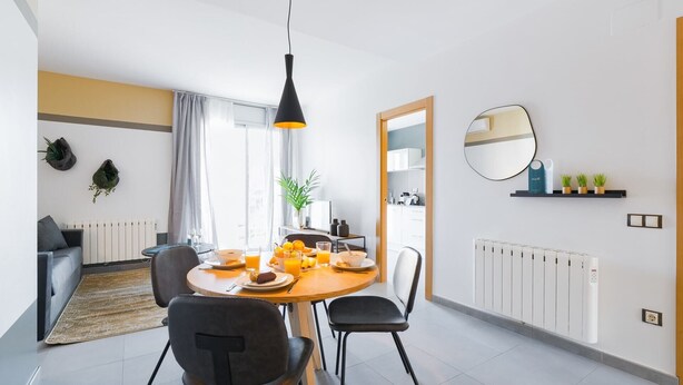 A modern dining area with a round table, two chairs, and a hanging pendant light. - Sweett | Callao III - Two Bedroom Apartment, Sleeps 4 (Barcelona)