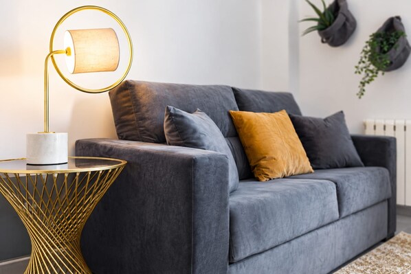 A modern living room with a grey sofa, a gold lamp, and a round side table. - Sweett | Callao III - Two Bedroom Apartment, Sleeps 4 (Barcelona)