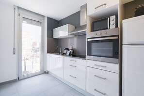 Une cuisine moderne avec des meubles blancs, un four à micro-ondes encastré, un four et une bouilloire posée sur le plan de travail.