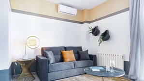 A modern living room with a grey sofa, a round coffee table, a small side table with a lamp, and a radiator. - Sweett | Callao III - Two Bedroom Apartment, Sleeps 4 (Barcelona)