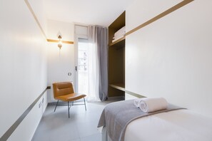 A hotel room with a bed, a chair, a wardrobe, and a window with curtains. - Sweett | Callao III - Two Bedroom Apartment, Sleeps 4 (Barcelona)