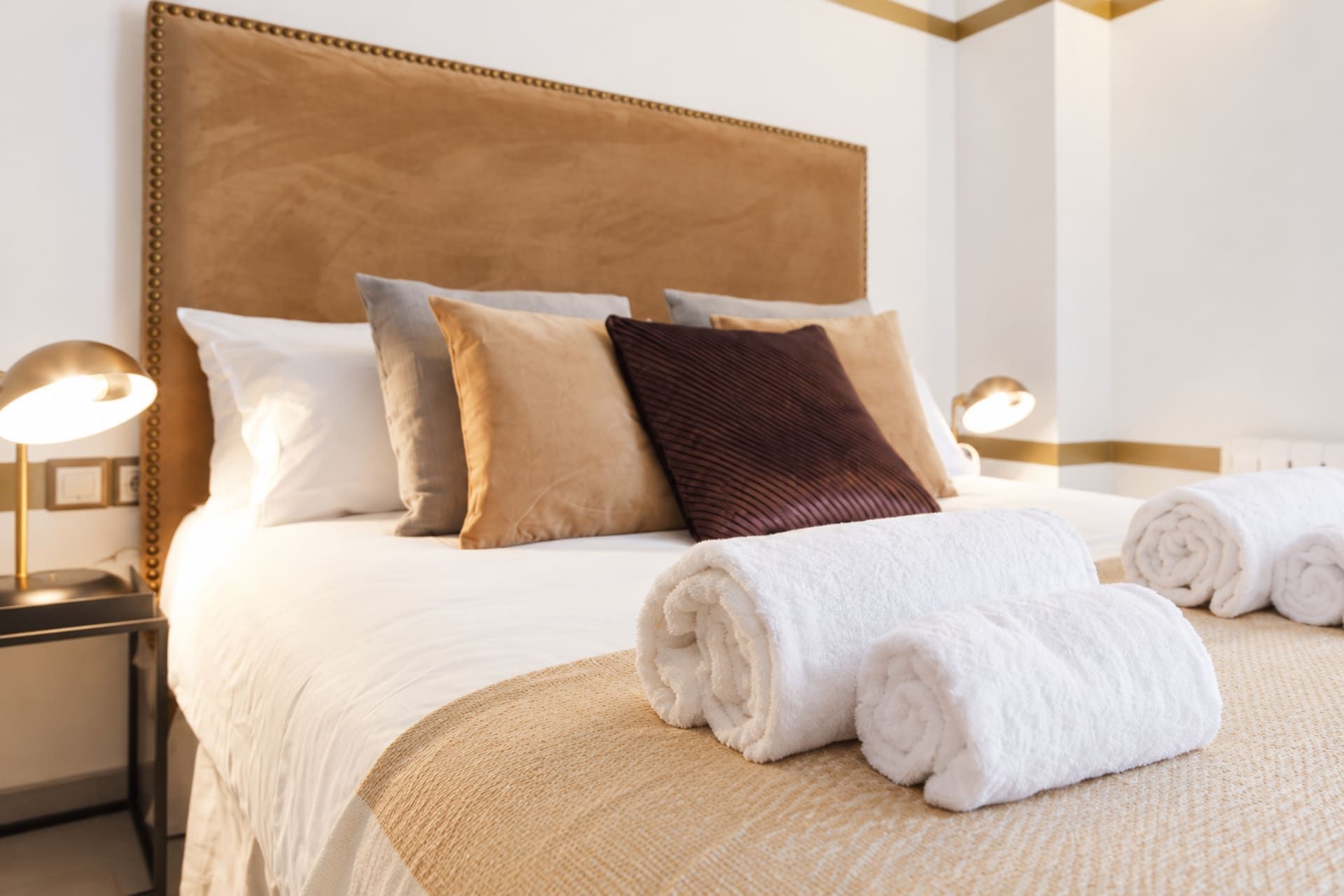 A neatly made bed with a headboard, pillows, and rolled towels.
