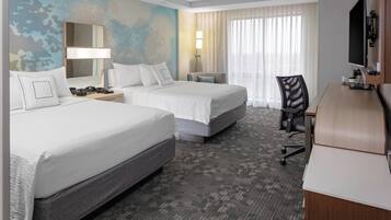 A hotel room with two beds, a desk, a chair, a TV, and a large window with curtains.