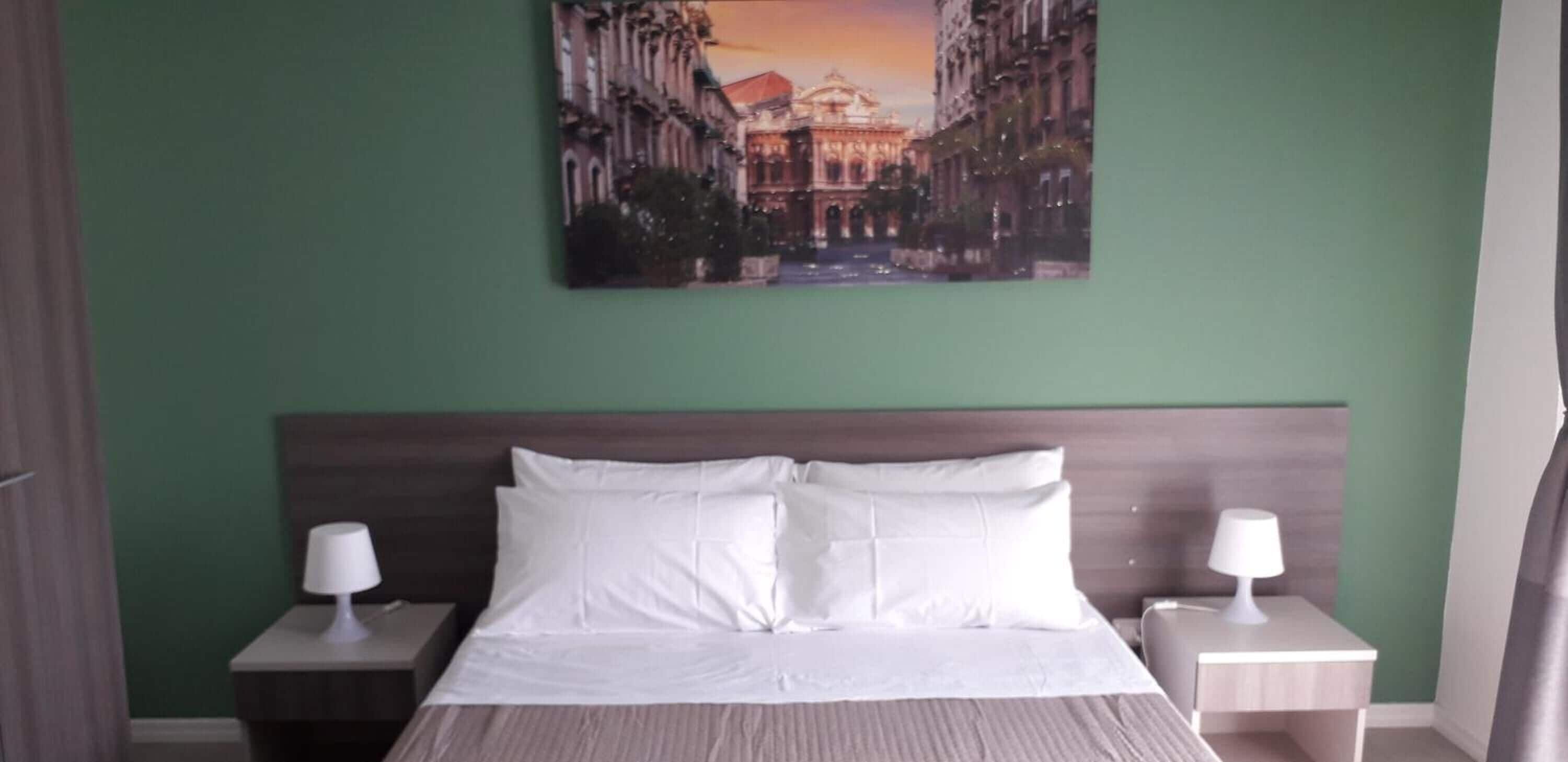 A hotel room with a bed, two bedside tables, and a painting of a cityscape on the wall.