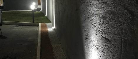 Una vista notturna di un edificio con una parete strutturata e un vialetto ben illuminato.