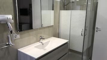 Un baño moderno con ducha de vidrio, lavamanos blanco y secador de pelo montado en la pared.