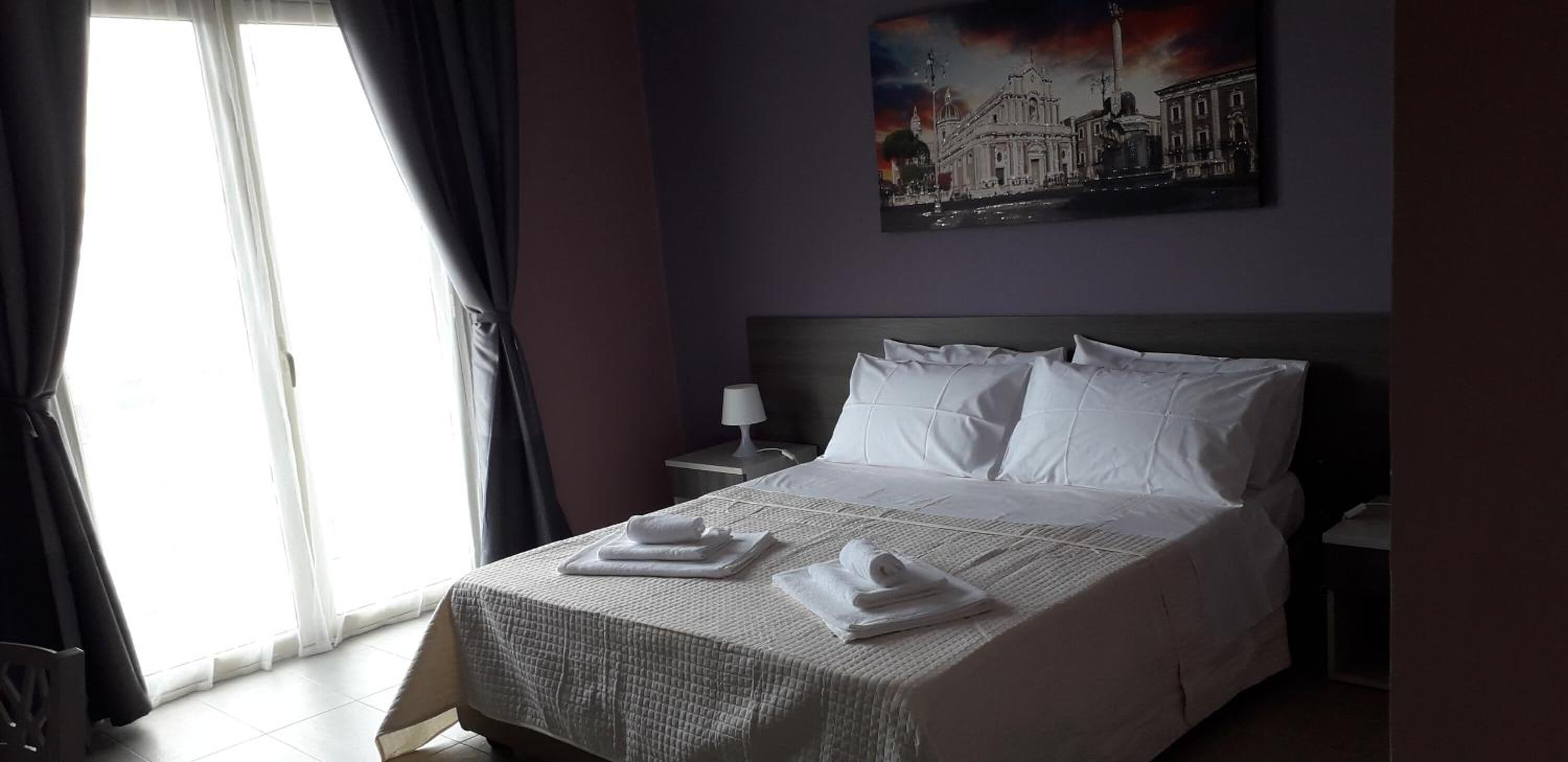 A hotel room with a bed, a nightstand, a lamp, and a painting on the wall.