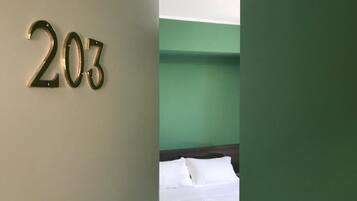 Una habitación con pared verde y cama con ropa de cama blanca.