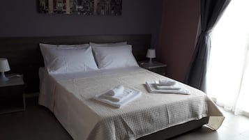 Una cama bien hecha con ropa blanca y toallas, un cabecero oscuro y una mesita de noche con una lámpara.
