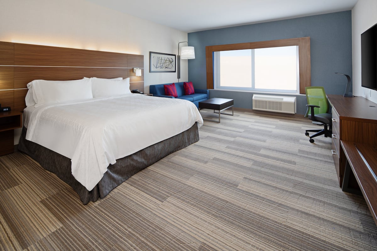 A hotel room with a large bed, a sofa, a desk, and a TV.