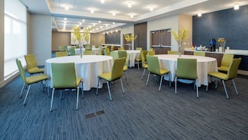 A conference room with multiple tables and chairs, equipped with ceiling lights and a projector screen.
