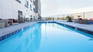 A swimming pool with a clear blue water surface, surrounded by a white building with multiple windows and a balcony area with wicker furniture. - Holiday Inn Express & Suites Murrieta by IHG (Murrieta)