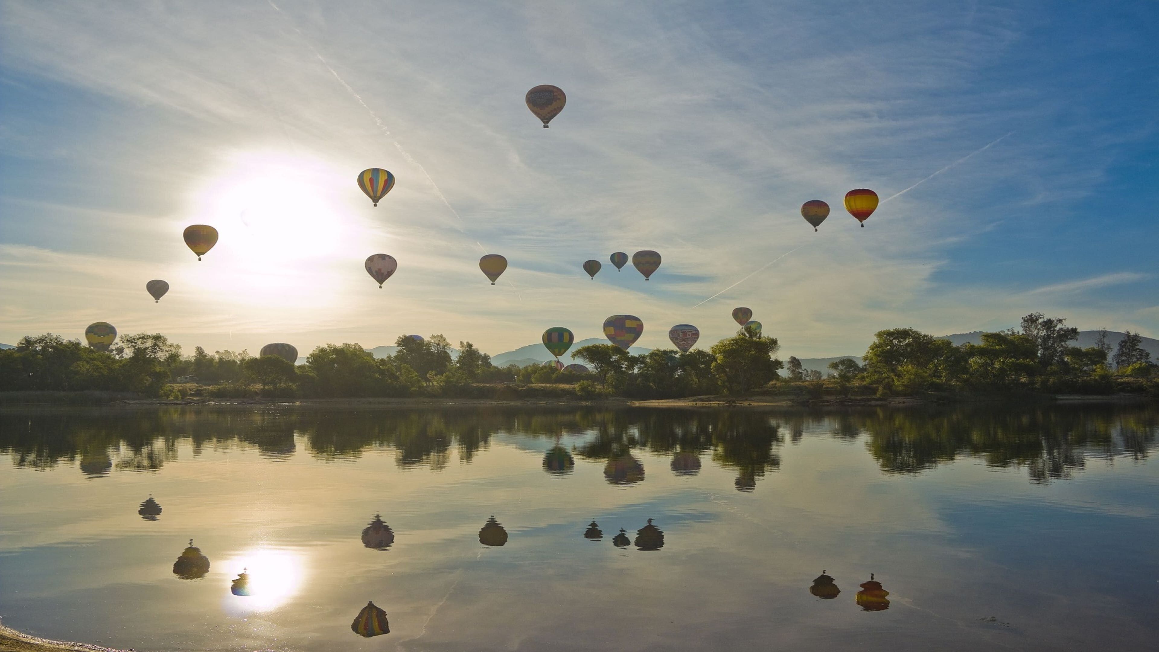 A calm body of water reflecting hot air balloons.