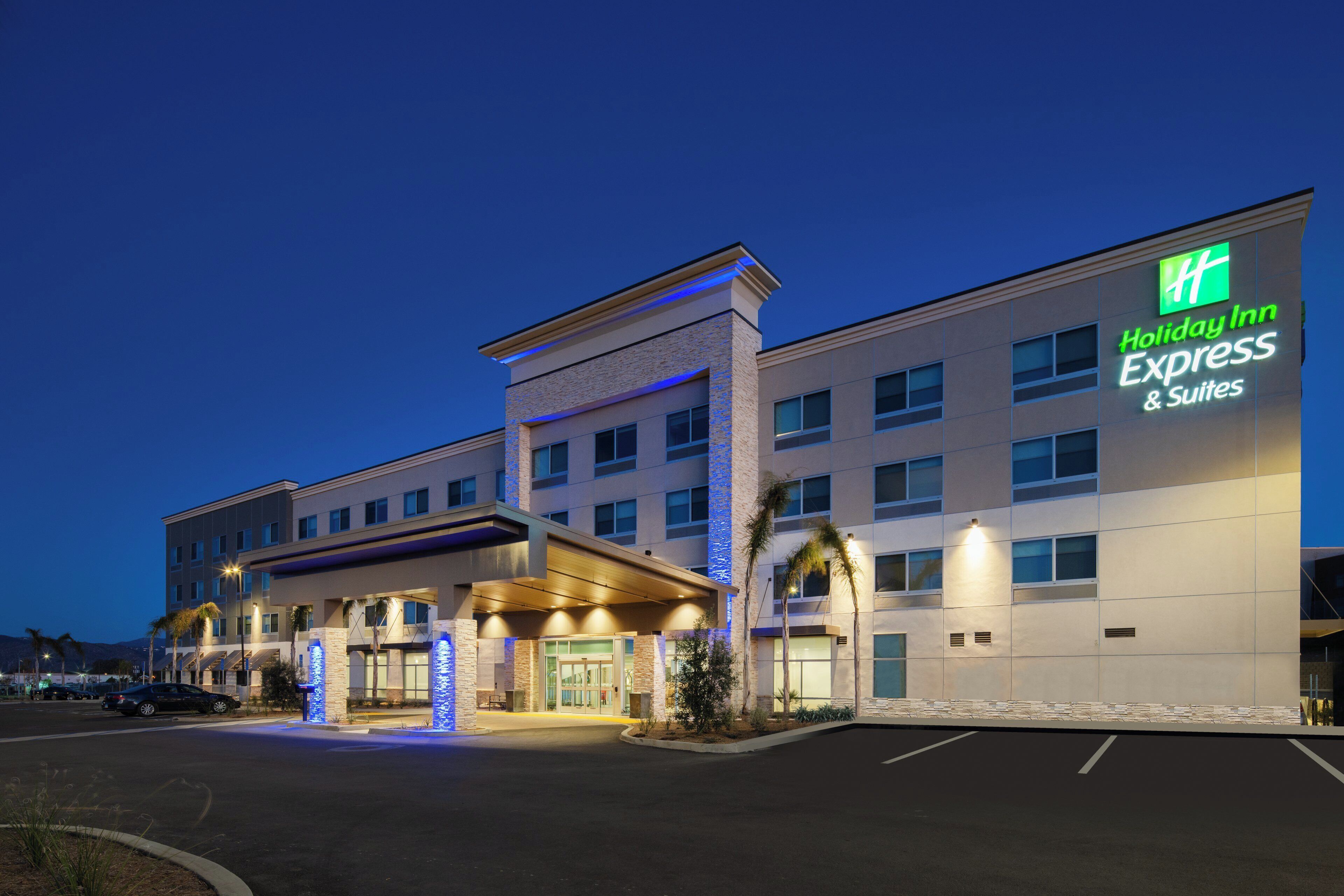 A Holiday Inn Express & Suites building with a modern design, featuring a prominent entrance with illuminated signage.