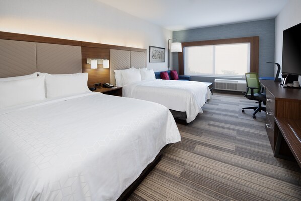 Een hotelkamer met twee bedden, een bureau, een stoel en een groot raam.