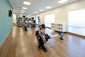 A gym with various exercise equipment, a wooden floor, and a large window providing natural light.