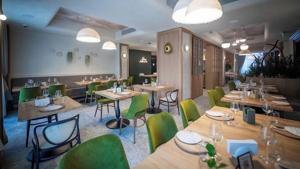 A modern restaurant with wooden tables and green chairs, pendant lighting, and a casual dining atmosphere. - Pensiunea Nora (Timisoara)