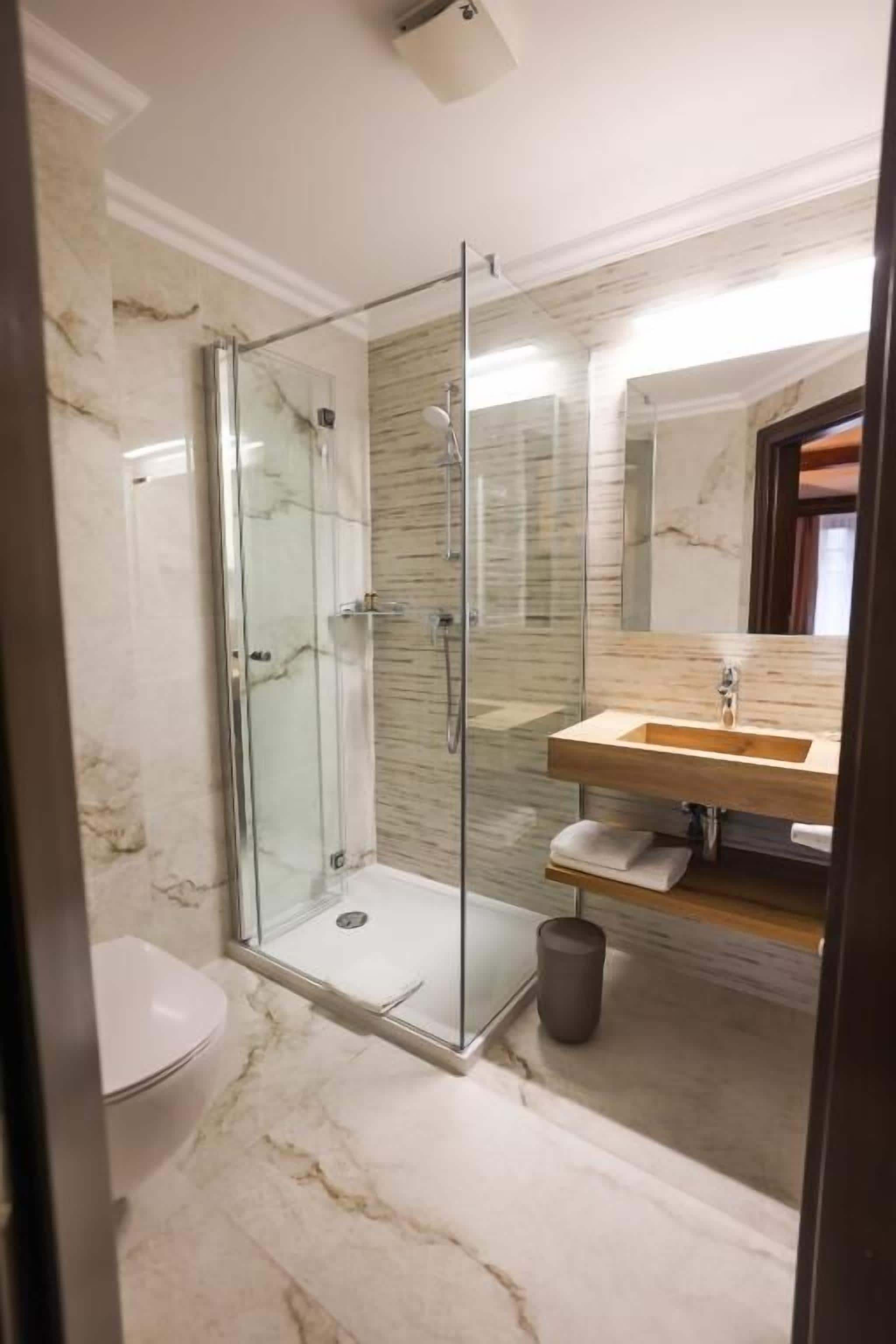 Ein Badezimmer mit einer Duschkabine aus Glas, einer Wand mit Marmorplatten, einem Holzboden und einer Toilette.