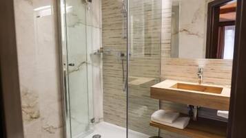 Ein Badezimmer mit einer Duschkabine aus Glas, einer Wand mit Marmorplatten, einem Holzboden und einer Toilette.