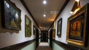 A hallway with framed artwork on the walls, a wooden floor, and a light fixture on the right. - Pensiunea Nora (Timisoara)