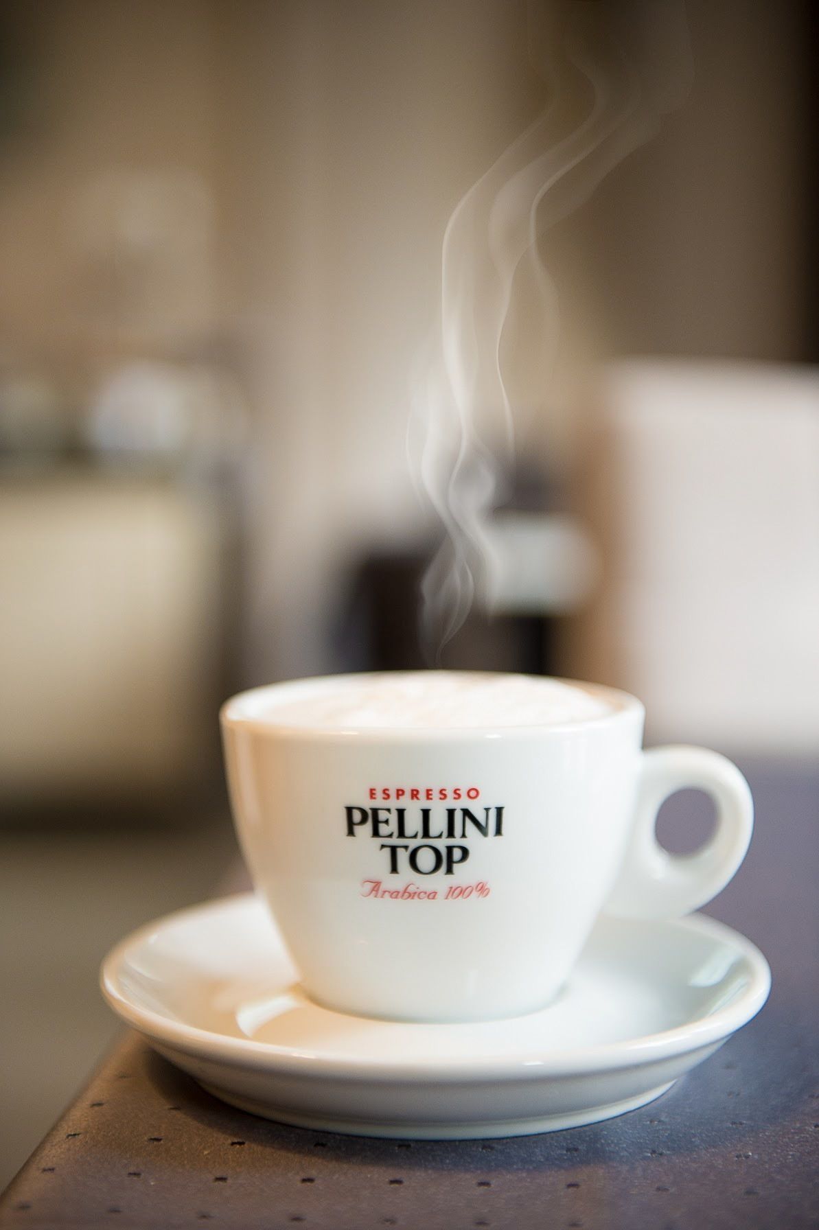 A white cup with steam, labeled "ESPRESSO PELLINI TOP Arabica 100%", on a saucer.