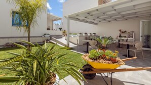 A patio area with a yellow wheelbarrow filled with plants, outdoor seating, and a white pergola. - Sirius (San Vito Lo Capo)