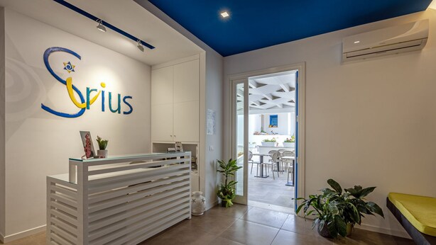 A reception area with a modern design, a reception desk, and a view into a dining area. - Sirius (San Vito Lo Capo)