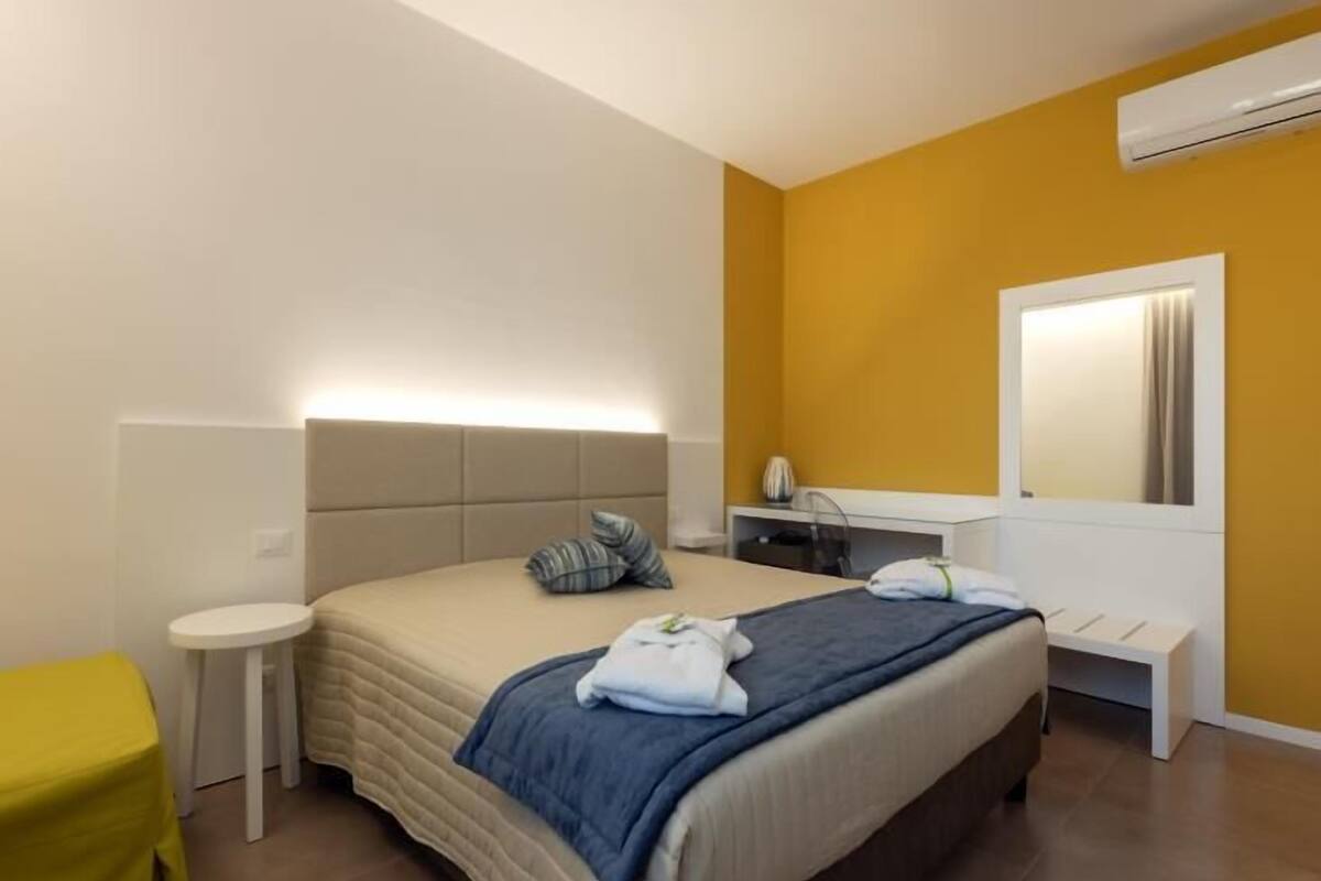 A modern hotel room with a bed, bedside table, and a small desk with a chair.