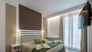 A modern hotel room with a large bed, bedside tables, a flat-screen TV, and a view of the outdoors through sheer curtains. - Sirius (San Vito Lo Capo)