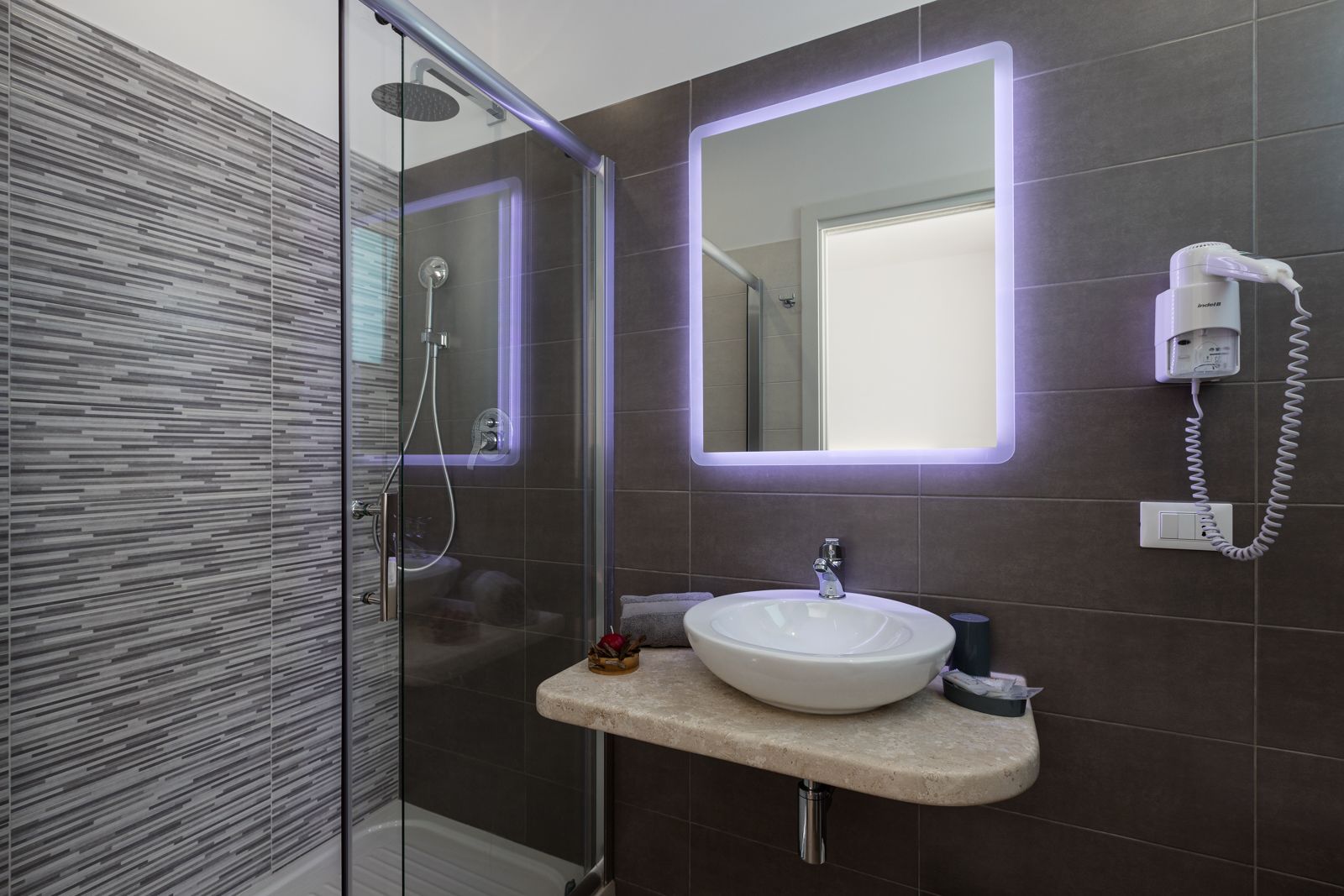 A modern bathroom with a glass shower enclosure, a white sink, and a hairdryer mounted on the wall.