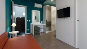 A modern interior with teal walls, a white door, a flat-screen TV, a desk, and a bench. - Sirius (San Vito Lo Capo)