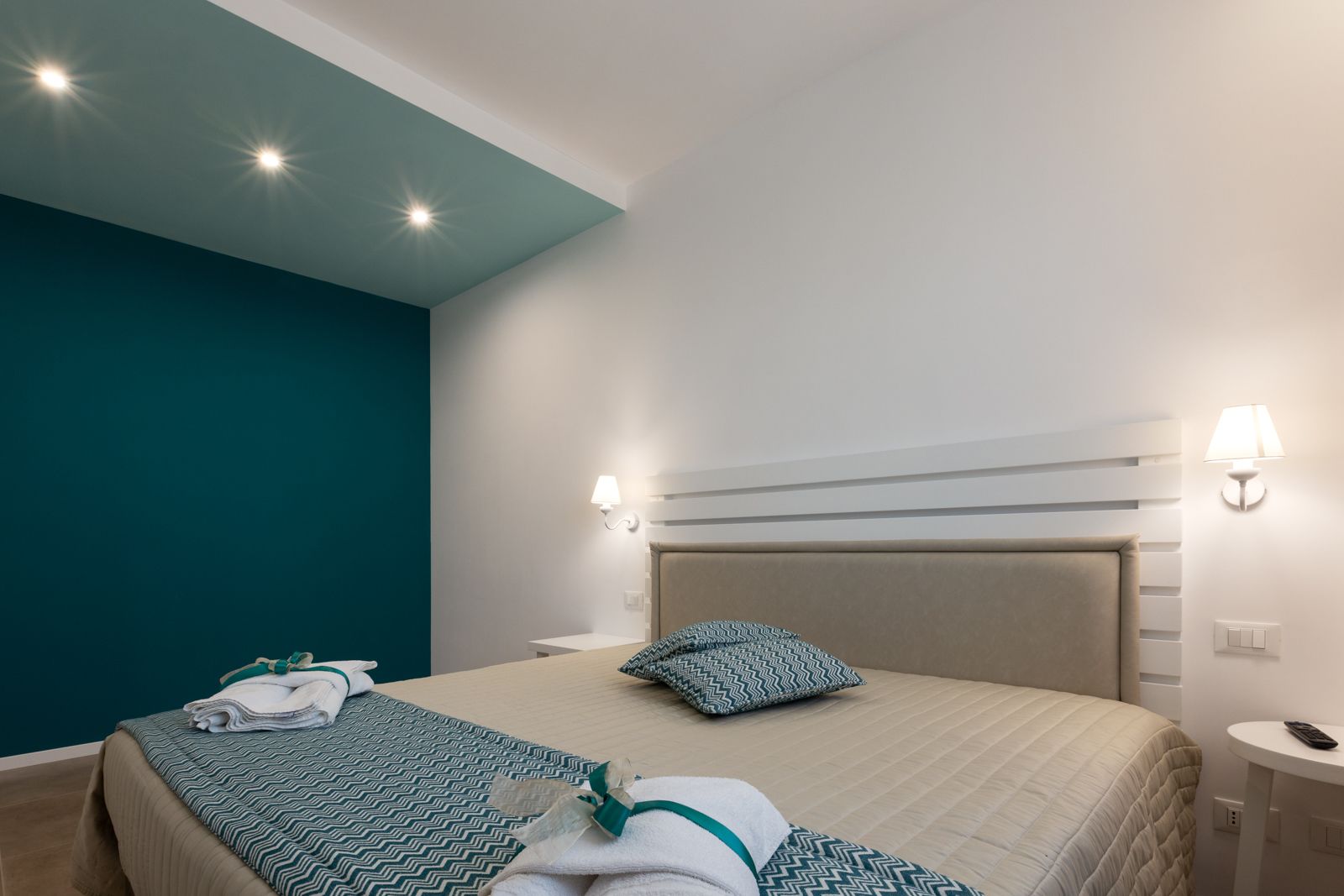 Una habitación de hotel con una cama, dos lámparas de noche, una mesita de noche y una luz de techo.