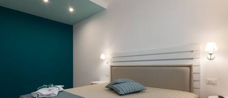 Una habitación de hotel con una cama, dos lámparas de noche, una mesita de noche y una luz de techo.
