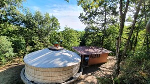 A round, covered outdoor structure with a small adjacent wooden building, surrounded by dense greenery. - Camping le P'Tit Bonheur (Escaro)