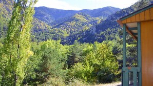 A rustic cabin with a wooden exterior and a green roof, surrounded by dense forest and mountains. - Camping le P'Tit Bonheur (Escaro)