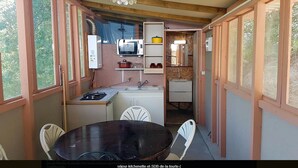 A compact kitchen with a microwave, stove, and sink, surrounded by white chairs and a table. - Camping le P'Tit Bonheur (Escaro)