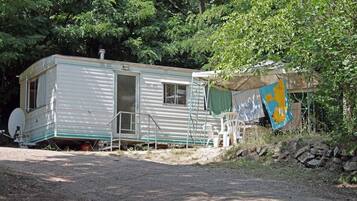 A mobile home with a satellite dish, a ladder, and a covered area with a flag.
