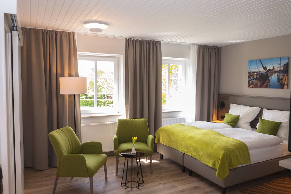 Una habitación de hotel con una cama, dos sillas, una mesa con un florero y un cuadro en la pared.