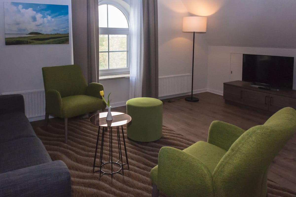 Una sala de estar con un sofá, dos sillones, una mesita con un florero, una lámpara y un televisor sobre un mueble bajo.