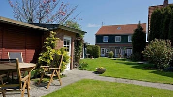 A residential property with a well-maintained lawn, a patio with a table and chairs, and a house with a red exterior and a green roof.