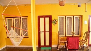 A room with a hammock, a dining table with chairs, and a door with a number. - Rajalakshmi Guest House (Tirukalukundram)