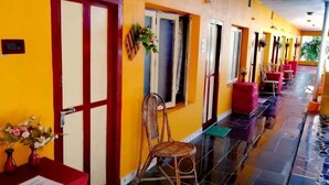 A hotel corridor with a yellow wall, red-framed doors, wicker chairs, and tables with red tablecloths. - Rajalakshmi Guest House (Tirukalukundram)