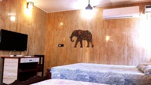 A hotel room with a marble wall, a flat-screen TV, a desk, a bed with a floral bedspread, and an elephant mural. - Rajalakshmi Guest House (Tirukalukundram)